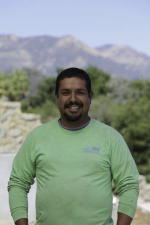 A man in a green shirt standing in front of a mountain.