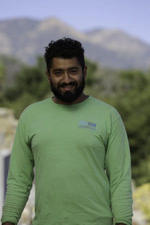 A man in a green shirt standing in front of a mountain.