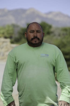 A man in a green shirt standing in front of a mountain.