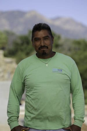 A man in a green shirt standing in front of a building.