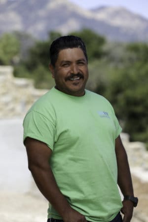 A man in a green shirt standing in front of a mountain.