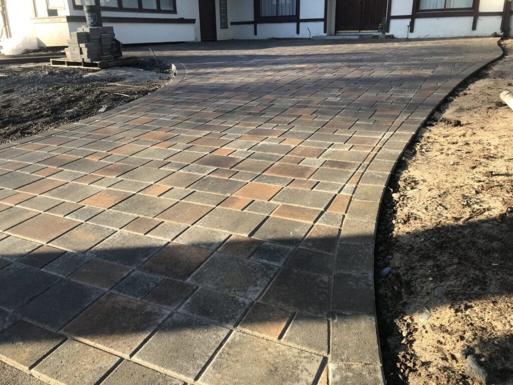 A newly installed paved driveway with large, multicolored rectangular stones leads up to the entrance of a house.